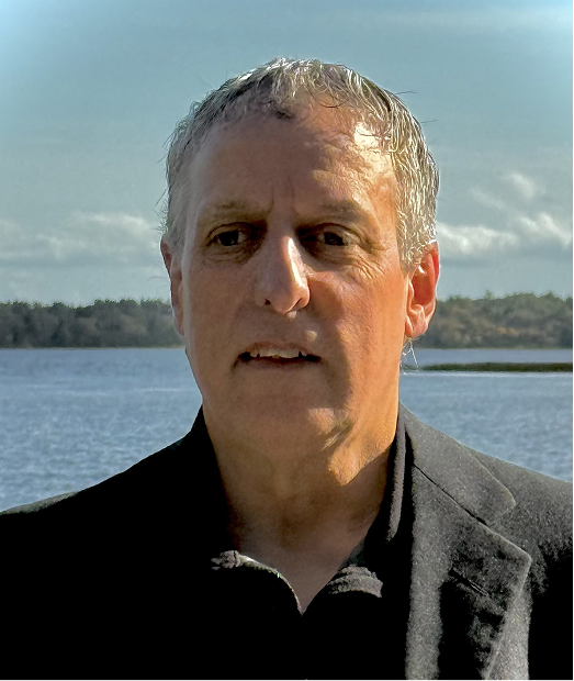Author G.H. Spears portrait – thoughtful headshot against a scenic lake backdrop, for Deconstructing America: Ideology, Decline & Path to Rebirth